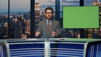A man in a suit speaks into a microphone in a television studio.
