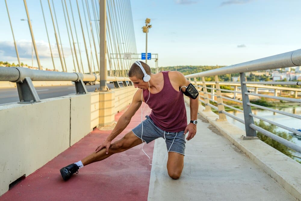 A man in athletic wear stretches his legs outdoors.