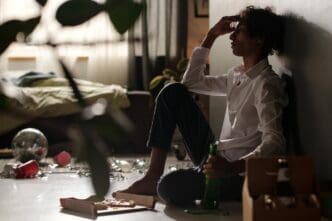 A teenage boy, looking pale and unwell, sits hunched over after a party.