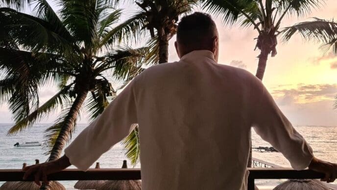 A man stands on a balcony overlooking a tropical ocean view.