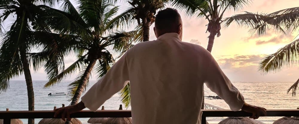 A man stands on a balcony overlooking a tropical ocean view.