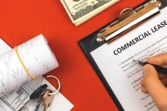 A man fills out a commercial lease agreement on a clipboard, next to house keys, a pen, and money, all against a red background.