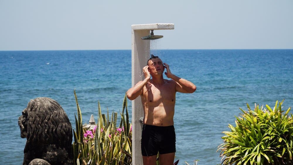 A man showers on a beach with the ocean in the background.
