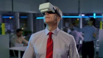 A mature businessman in a suit wears virtual reality goggles in a modern office setting.