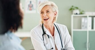 A mature female doctor and patient laugh together during a medical consultation.