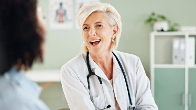 A mature female doctor and patient laugh together during a medical consultation.