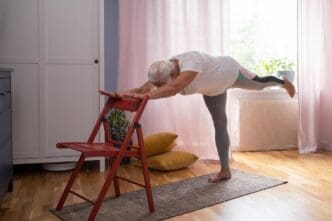 A mature woman in casual clothing practices yoga at home.