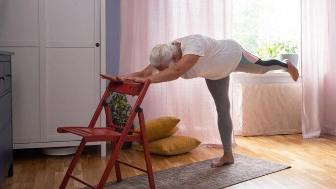 A mature woman in casual clothing practices yoga at home.