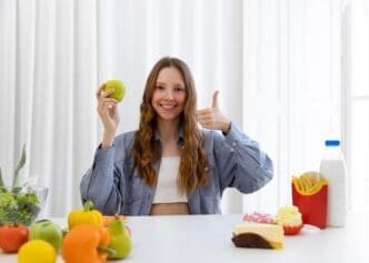 A woman in a medium shot holds an apple and gives a thumbs-up gesture.