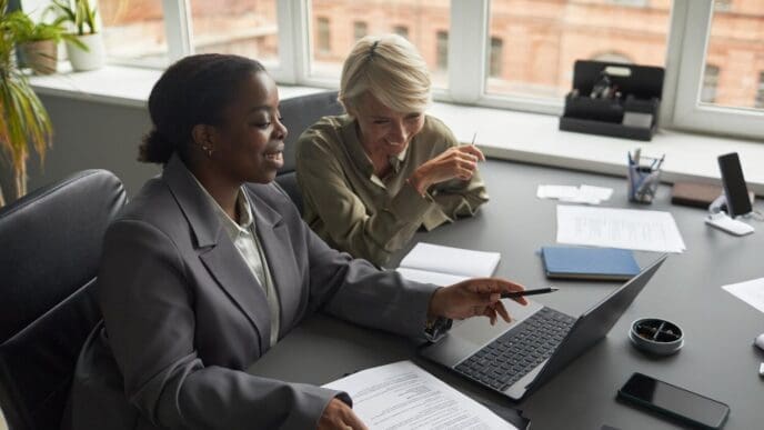 A middle-aged white woman and a young Black woman are working together, likely at a job.