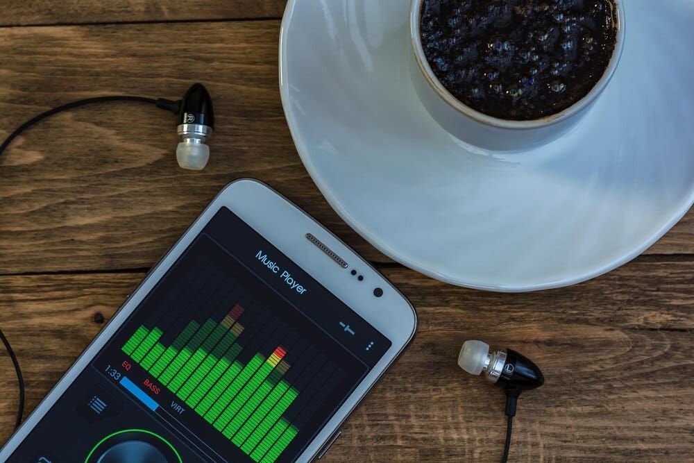 A close-up shows a mobile phone displaying an equalizer next to a cup of coffee on a saucer.