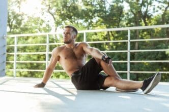 A muscular man with a naked torso stretches outdoors.