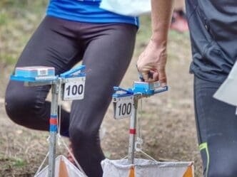 A person wearing a bib is reaching for a check point marker during an outdoor orienteering race.