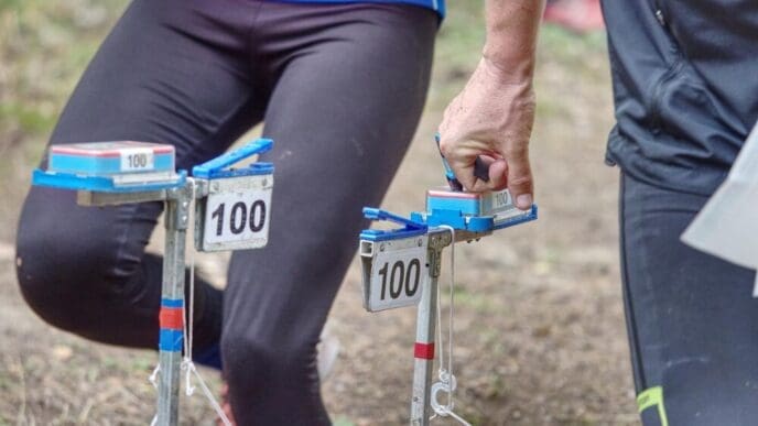 A person wearing a bib is reaching for a check point marker during an outdoor orienteering race.