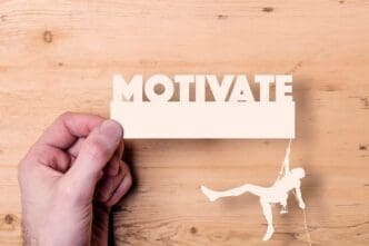 A paper cutout shows a climber reaching for the word "motivate," representing a business concept.