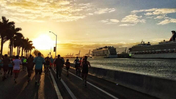 People run along a road in Miami Beach during a sunrise, silhouetted against the sky.