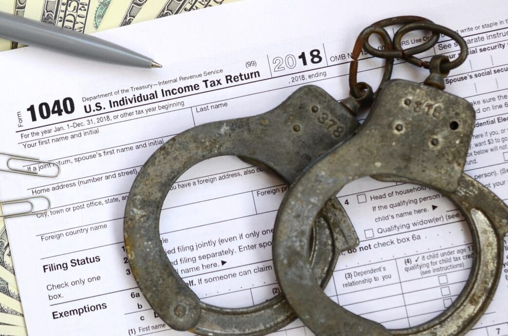 Police handcuffs rest on a completed IRS 1040 tax form.
