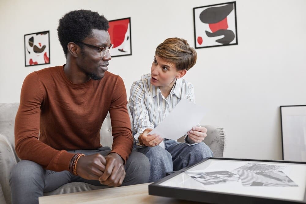 An African-American man and a female art gallery manager discuss paintings while planning an exhibition in a museum.