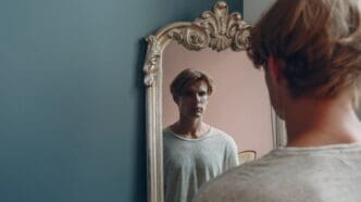 Portrait of a young European man looking at a mirror in an indoor studio setting.