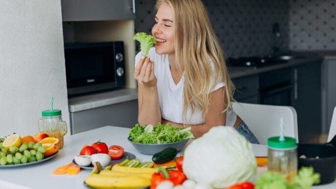 A smiling woman sits at a table, enjoying a healthy meal.