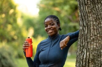 Smiling Black female athlete holds a water bottle while training outside.