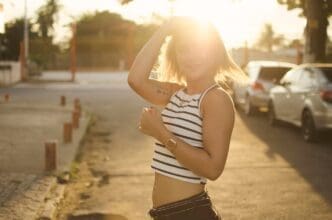 A woman with her hand in her hair smiles while standing in a city.