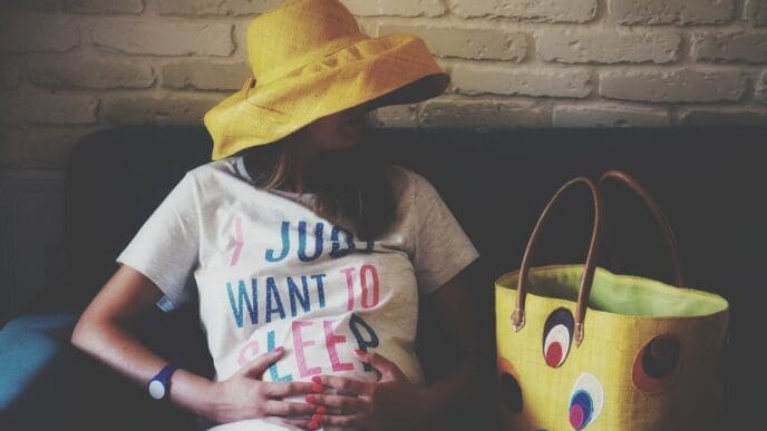 A pregnant woman sits on a sofa, positioned against a wall.