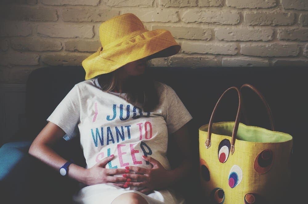A pregnant woman sits on a sofa, positioned against a wall.