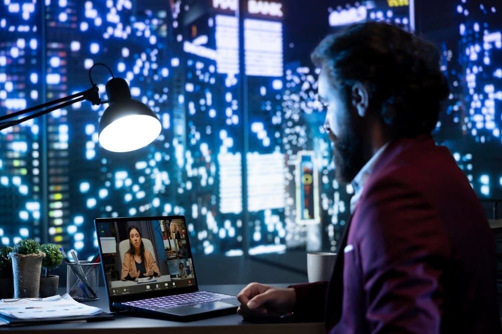 A person wearing a suit and tie speaks to a group of people on a computer screen during a video conference.