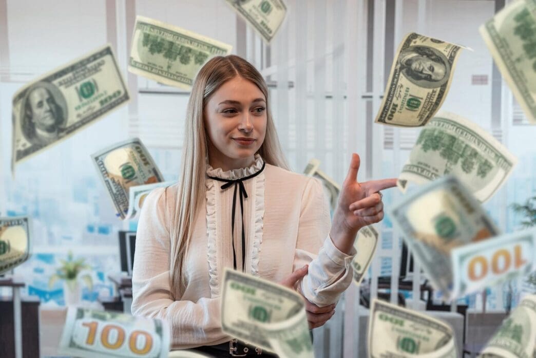 A smiling Caucasian woman celebrates with dollar bills floating around her.