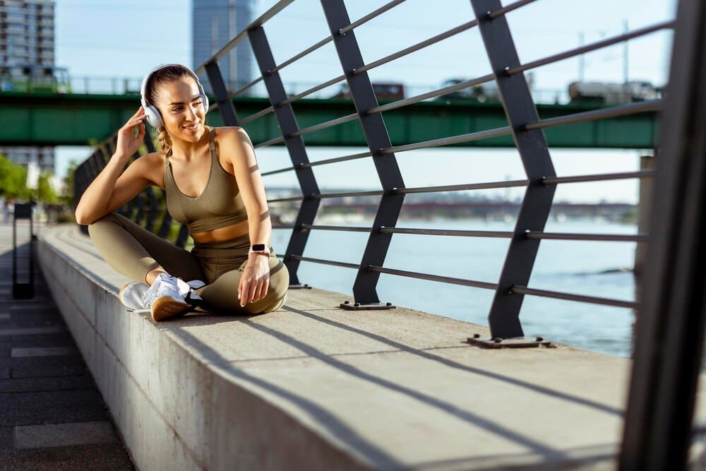 A young woman with earphones takes a break after running in an urban area.
