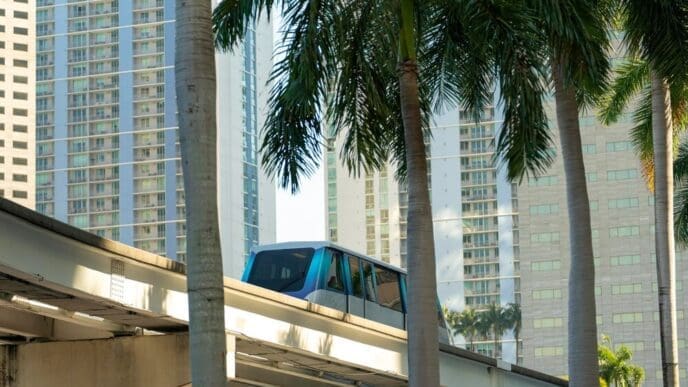 A Metrorail train car travels on an elevated track between skyscrapers in downtown Miami, Florida.