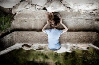 Rear view of a woman lying on a footpath, looking into a dark tunnel.