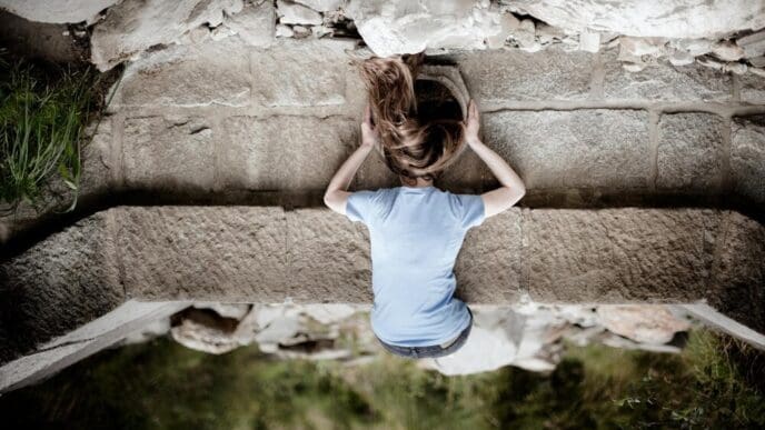 Rear view of a woman lying on a footpath, looking into a dark tunnel.
