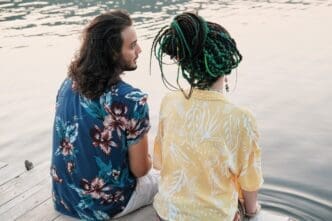 Rear view of a young couple sitting on a pier, dipping their feet in the water, and talking.