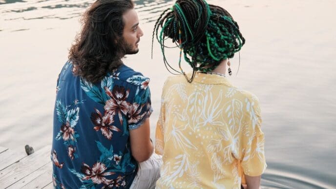Rear view of a young couple sitting on a pier, dipping their feet in the water, and talking.