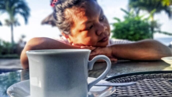A woman sits alone, looking down at a cup in her hands, conveying sadness.