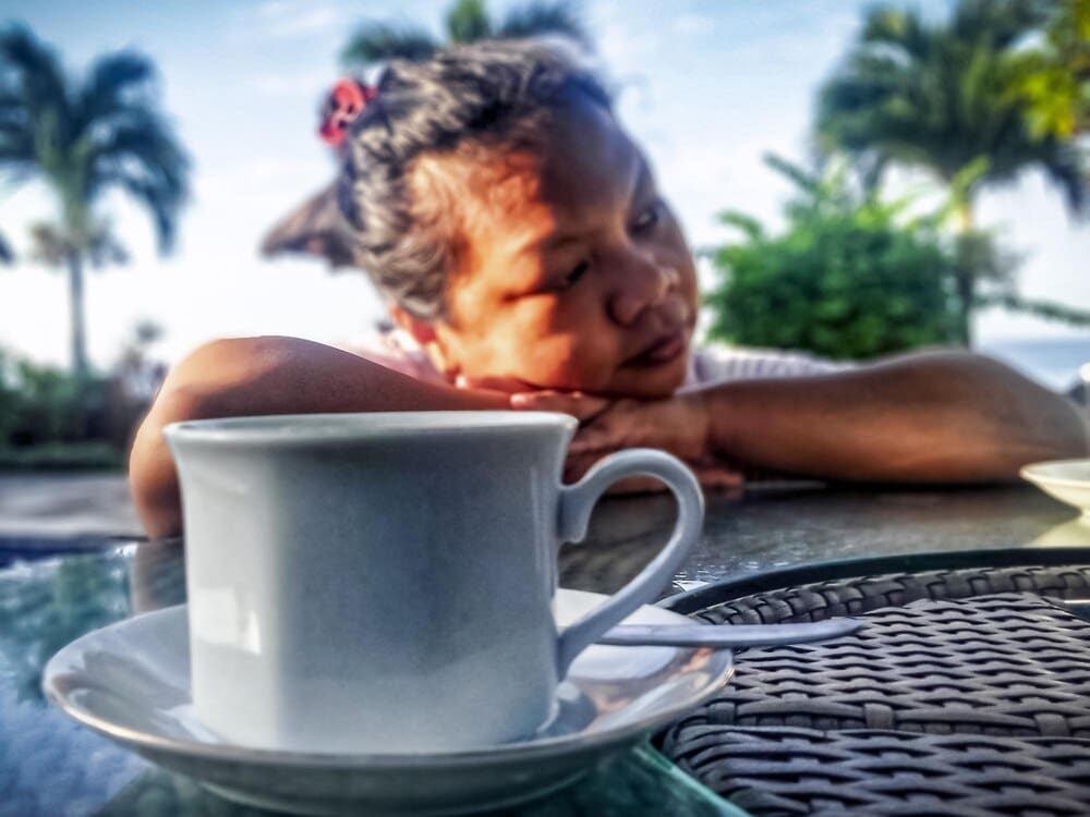 A woman sits alone, looking down at a cup in her hands, conveying sadness.