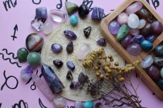 Amethyst runes and dried herbs are arranged on a pink surface.