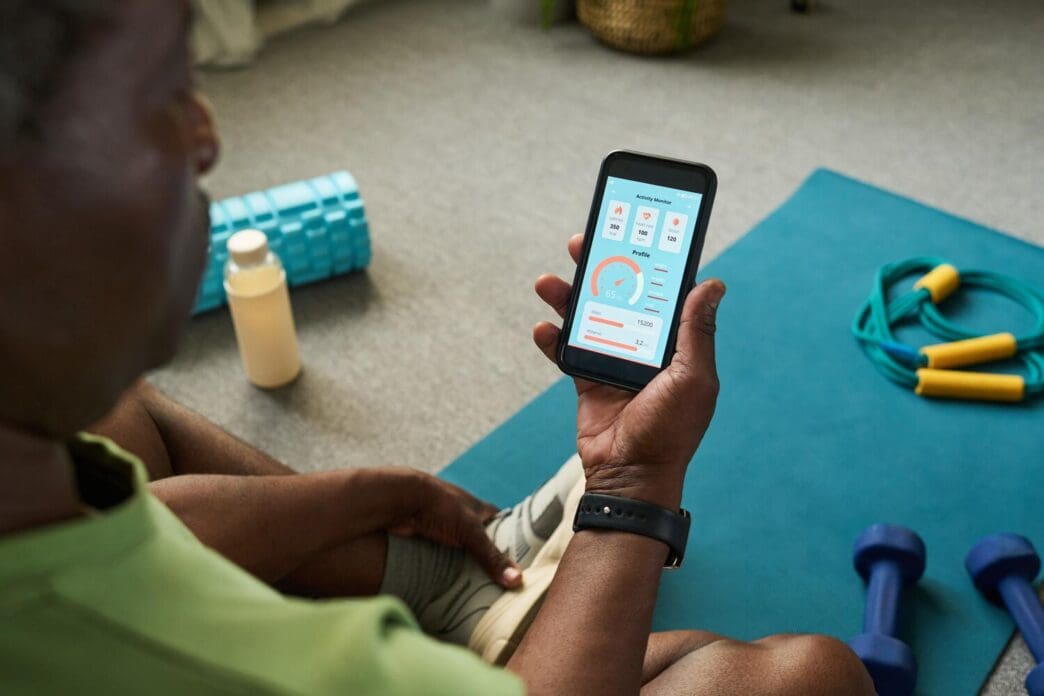 Senior Black man using a smartphone to follow a fitness app while working out at home.