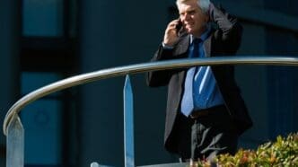 A senior businessman in a suit stands on a city street, likely representing business or financial concepts.