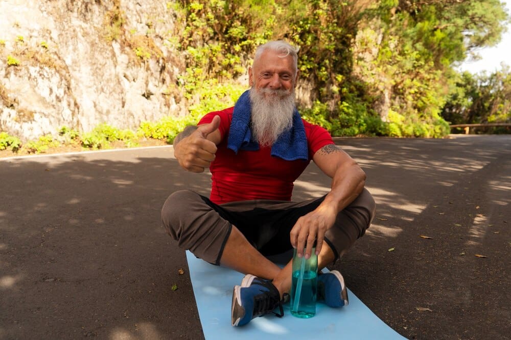 A senior man with a white beard smiles while exercising outdoors.