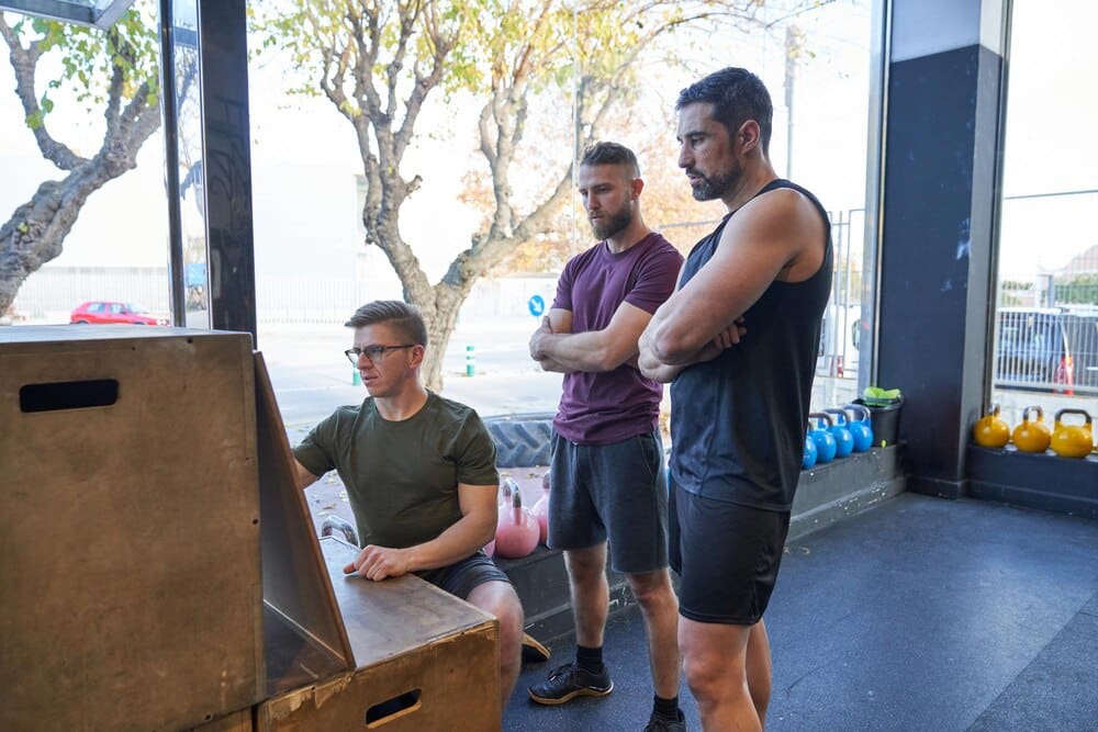 Side view of two male athletes in sportswear preparing for a workout in a modern gym with glass walls and sports equipment.