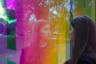 A woman with mid-length hair gazes out a vibrant, multi-colored window.