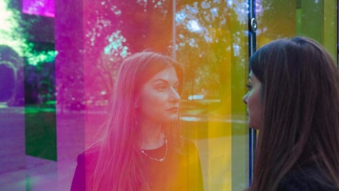 A woman with mid-length hair gazes out a vibrant, multi-colored window.