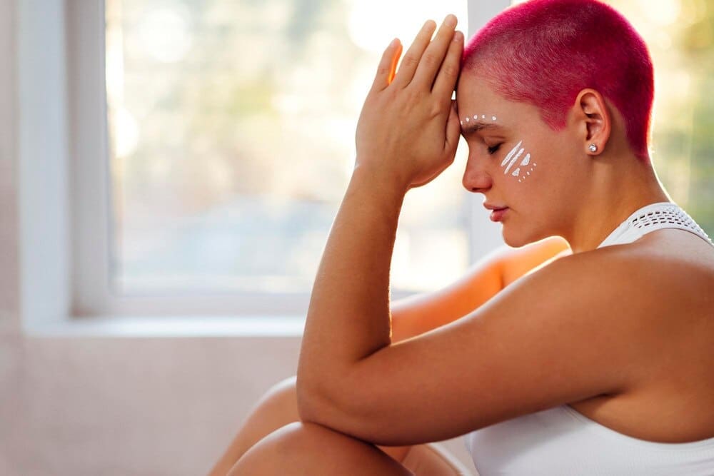 Side view of a young woman with bare shoulders sitting on a bed.
