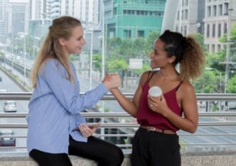 Side view of smiling women holding hands by a railing.