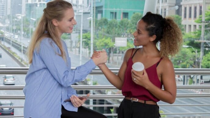 Side view of smiling women holding hands by a railing.