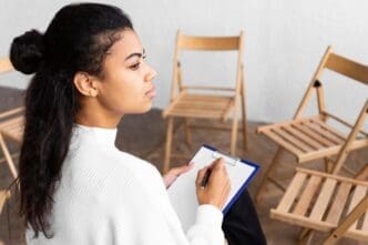 Woman in profile, holding a clipboard, participates in a group therapy session.