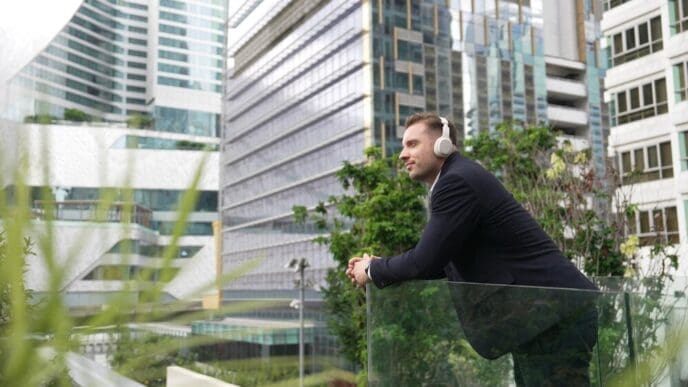 A businessman wearing headphones stands on a rooftop, likely enjoying music in an urban setting.